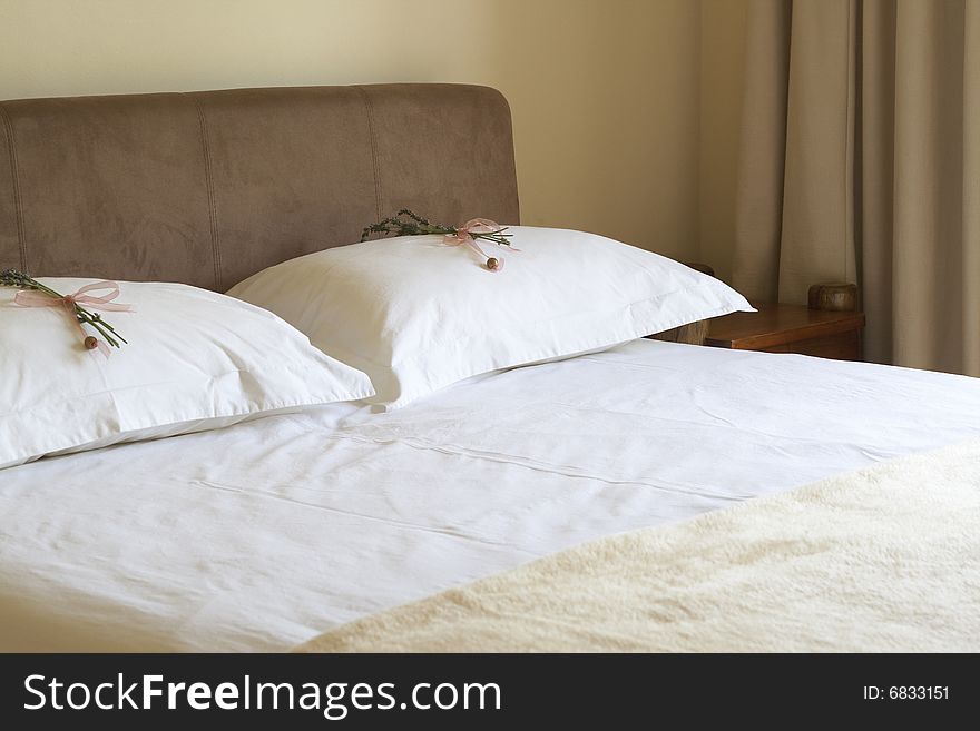 Beautiful bedroom interior with white sheets and flower decorations on pillows. Warm tone