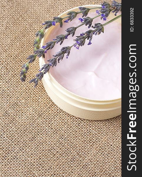 Relaxing spa scene with pink body butter in a jar and some lavender stems on mesh material bacground with copy space