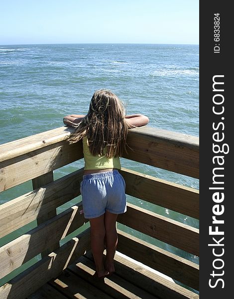 Young brunette girl staring out over the ocean from wooden jetty,seen from behind. Young brunette girl staring out over the ocean from wooden jetty,seen from behind