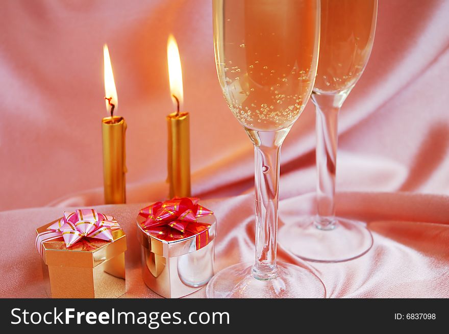 Pair of champagne flutes with candles and gift box on silk background