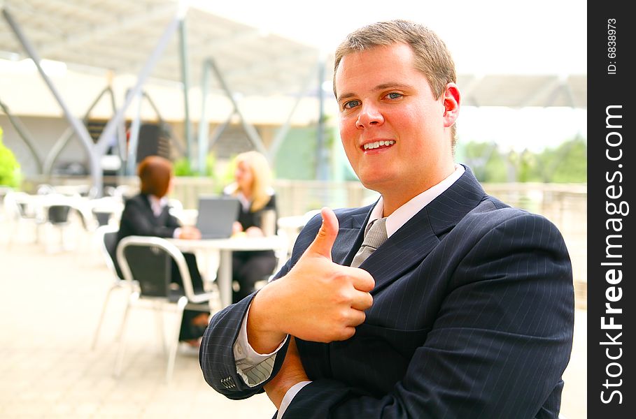 Business man giving ok sign or thumb up with happy expression. two other business women on the background. Business man giving ok sign or thumb up with happy expression. two other business women on the background