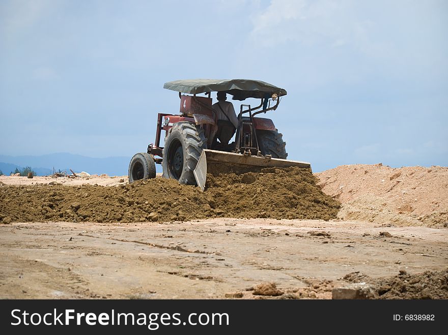 A construction worker moving dirt with a tractor during a hot sunny afternoon. A construction worker moving dirt with a tractor during a hot sunny afternoon