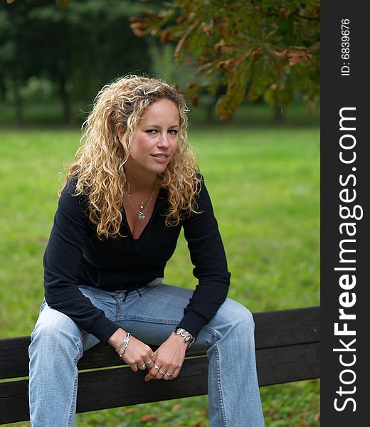 Curly girl sitting on bench in park. Curly girl sitting on bench in park
