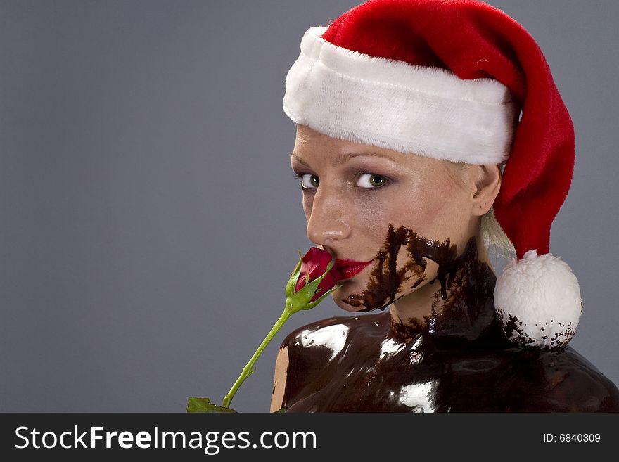Attractive naked blond girl covered in chocolate wearing a santa hat and holding red rose. Attractive naked blond girl covered in chocolate wearing a santa hat and holding red rose
