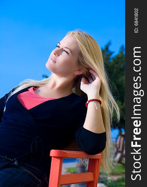 Beautiful blondy sitting on red chair  in sun
