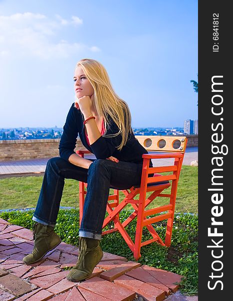 Beautiful blondy sitting on red chair  in sun