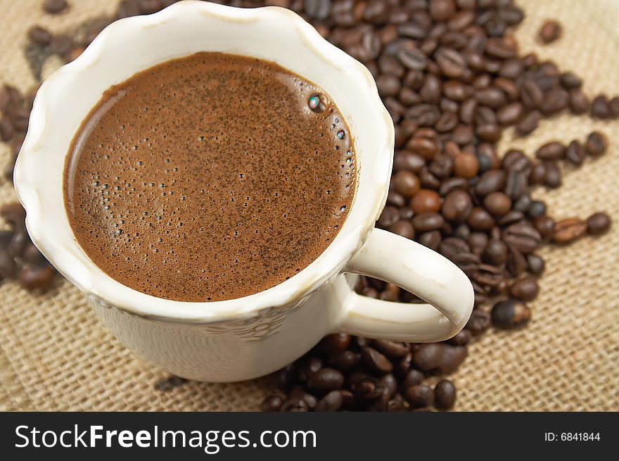 Cup of aromatic coffee and coffee beans on webbing material. Cup of aromatic coffee and coffee beans on webbing material