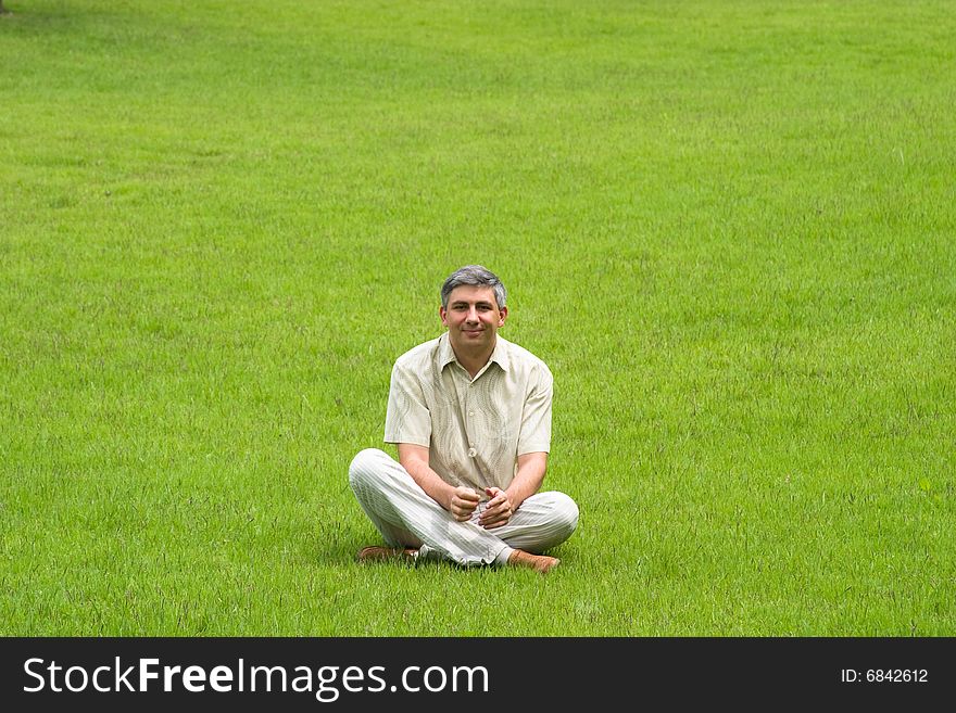 Smiling man sitting on grass field. Smiling man sitting on grass field