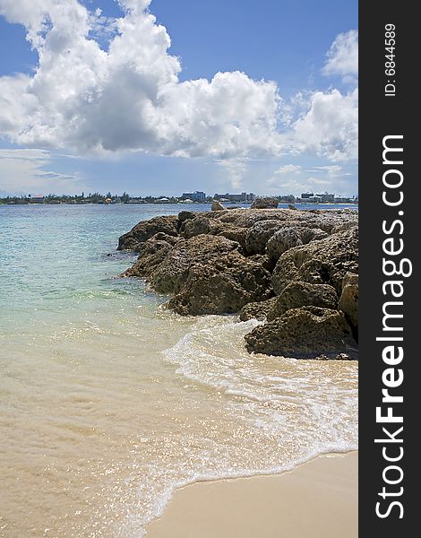 Tropical beach with rocks extending into the clear blue water.