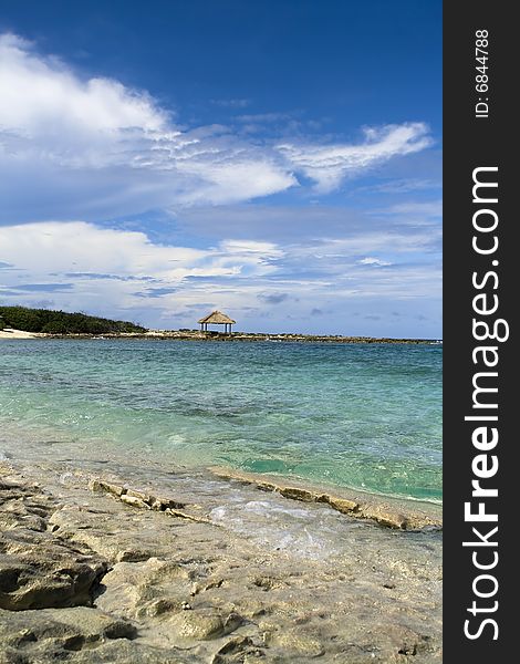 Tropical shoreline with clear green water and beach hut off in the distance. Tropical shoreline with clear green water and beach hut off in the distance.