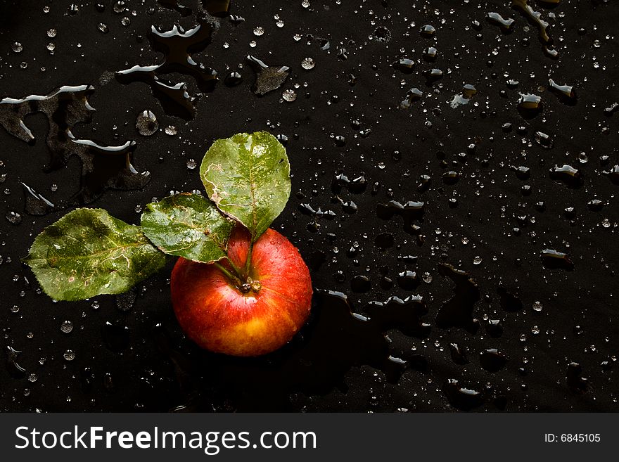 Wet red apple with green leafs on a bladk background. Wet red apple with green leafs on a bladk background