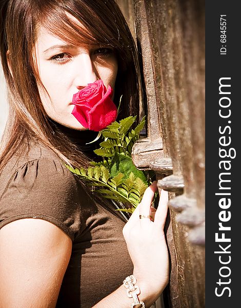 Young woman smelling a red rose over metal fence. Young woman smelling a red rose over metal fence.