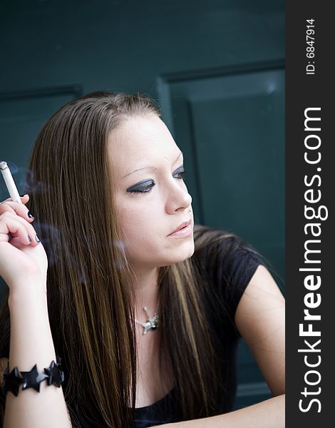 Young woman smoking a cigarette, lost in thought, as she sits on a doorstep