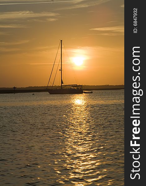 Sailboat anchored in a harbor at sunset. Silloutting of boat and bay features by setting sun. Sailboat anchored in a harbor at sunset. Silloutting of boat and bay features by setting sun.