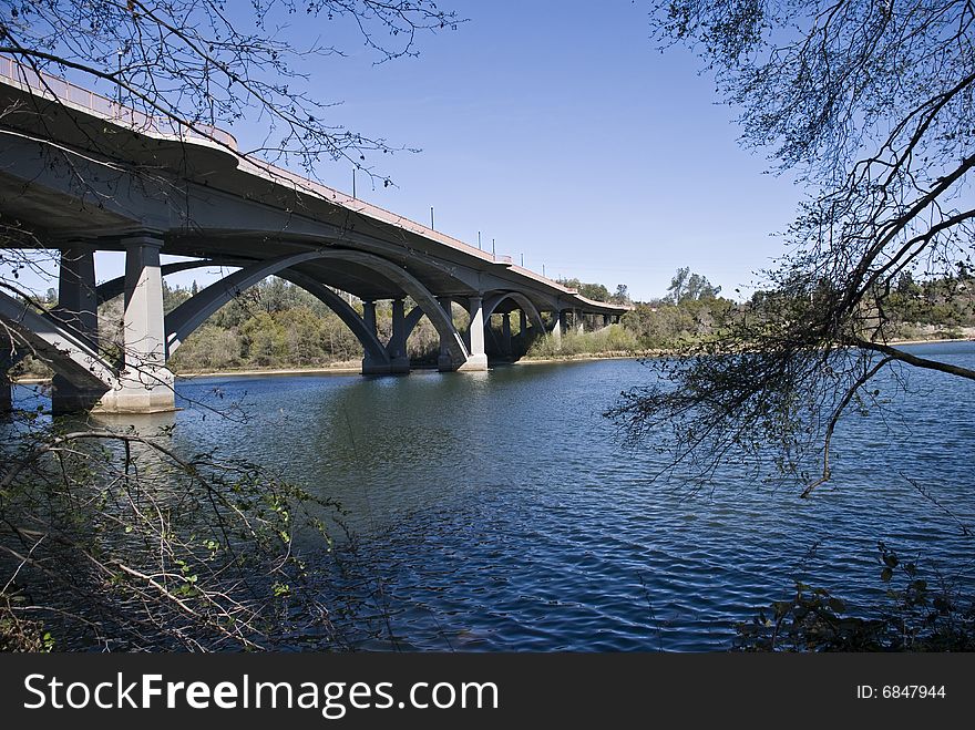 Cement bridge over river with trees and blue sky and water