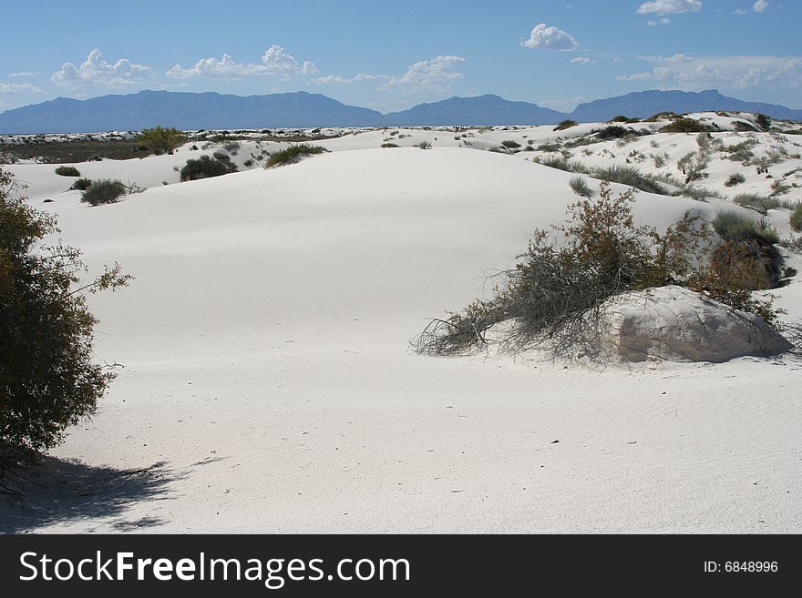 Scenic view of White Sands National Park with bushes, mountains, and clounds in the sky. Scenic view of White Sands National Park with bushes, mountains, and clounds in the sky.