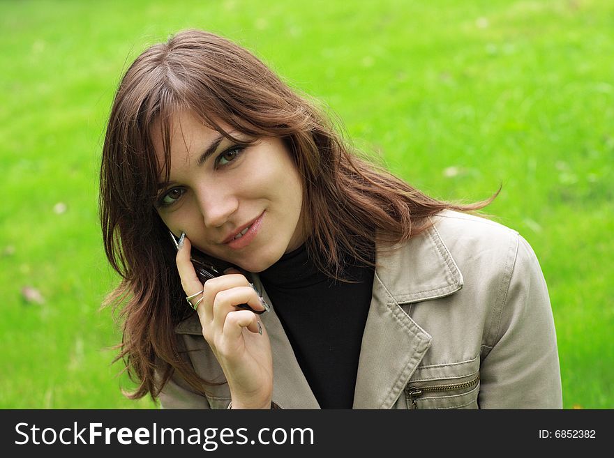Beautiful young girl with a phone, over green grass background