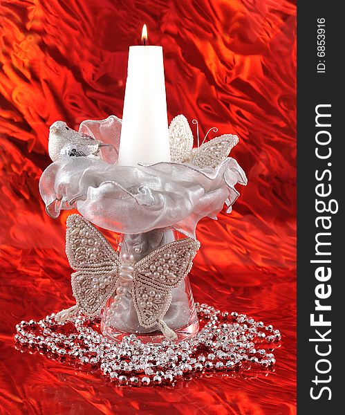 Tall christmas composition with silver baterflies, bird, ribbons, beads and lit candle on shiny red background. Tall christmas composition with silver baterflies, bird, ribbons, beads and lit candle on shiny red background