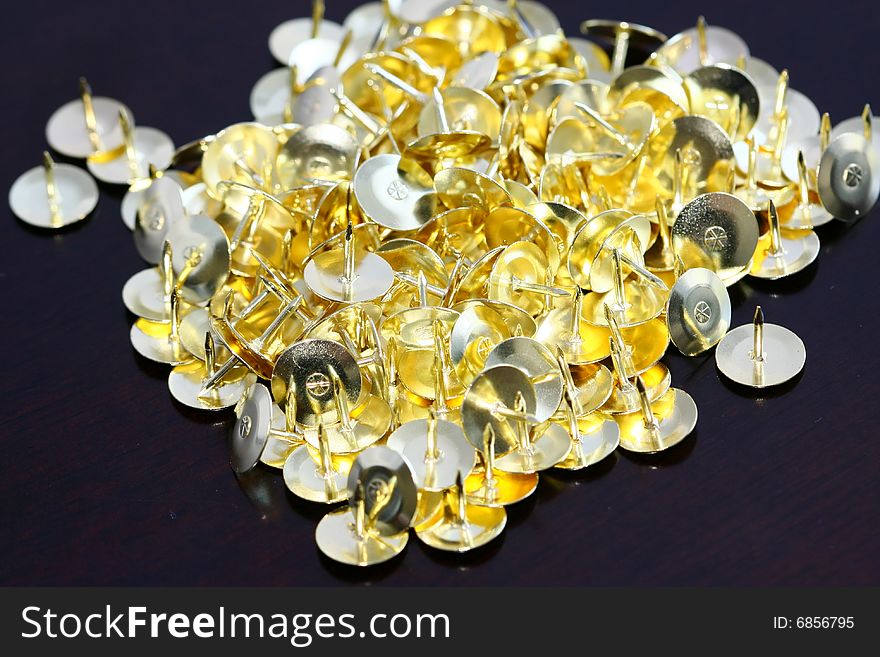 Macro photography of golden drawing pins on dark brown table top