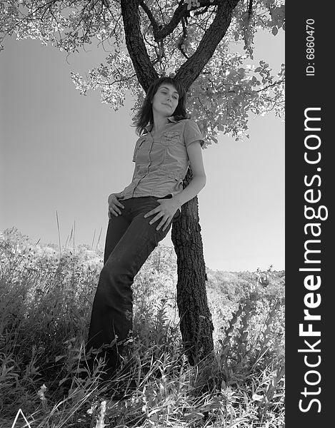 The girl in the field leans against a tree. Monochrome