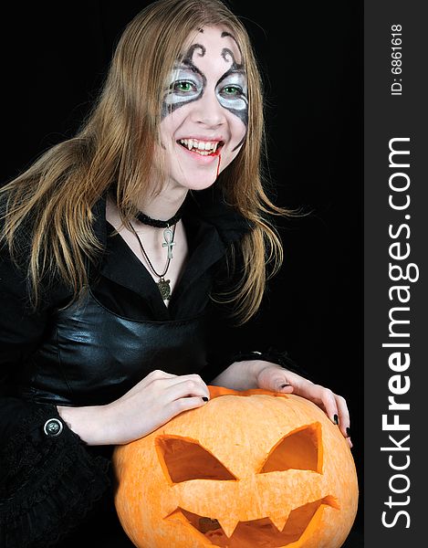 Laughing vampire girl with halloween pumpkin, on black background