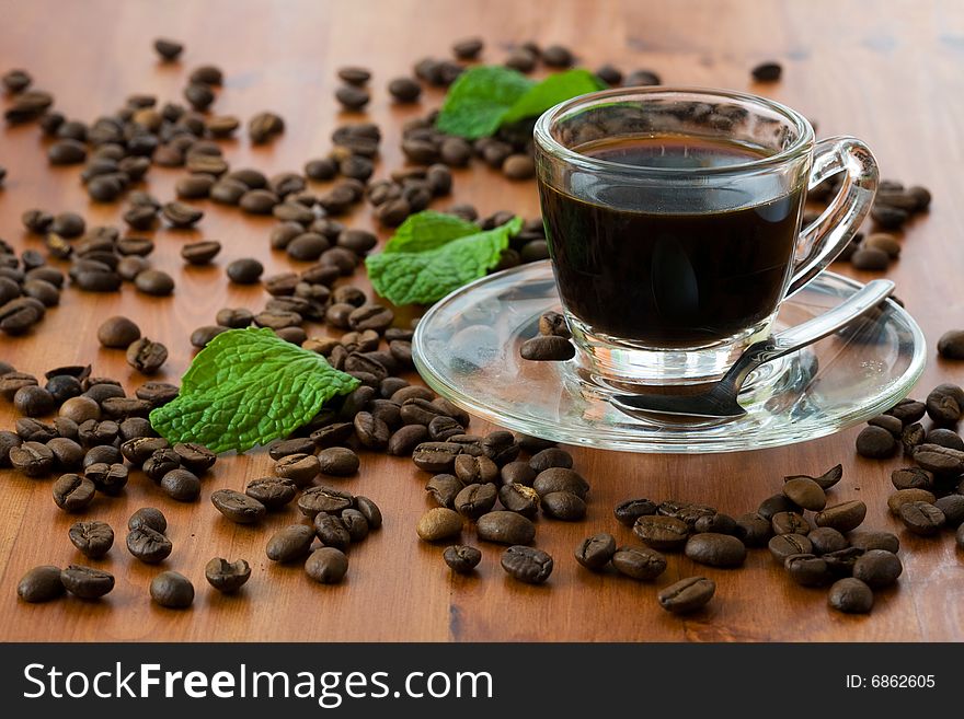 A cup of dark coffee with beans over wood background