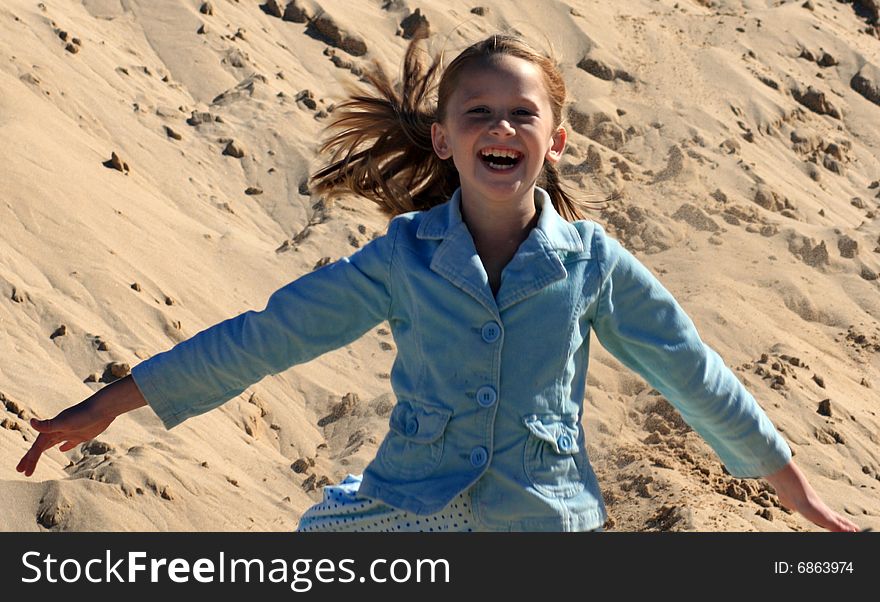 A white caucasian girl child running down a sand dune on a hot summers day with a happy expression on her pretty face. A white caucasian girl child running down a sand dune on a hot summers day with a happy expression on her pretty face