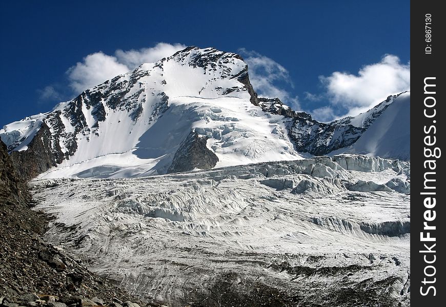 South face of Dom - highest mountain within Switzerland, covered with snow, under blue sky and white clouds, above glacier. South face of Dom - highest mountain within Switzerland, covered with snow, under blue sky and white clouds, above glacier