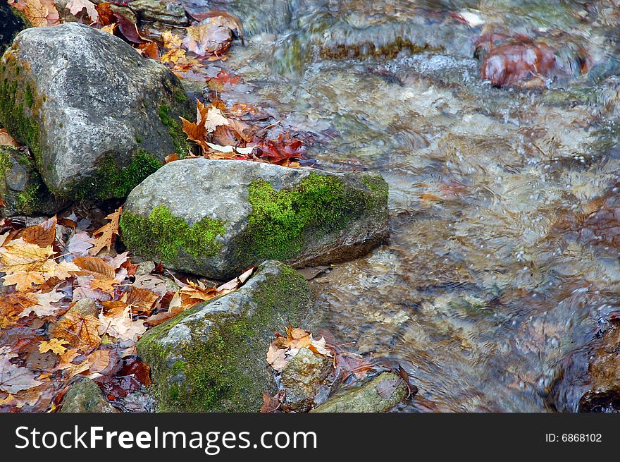 Moss-covered rocks next to a rippling stream. Moss-covered rocks next to a rippling stream