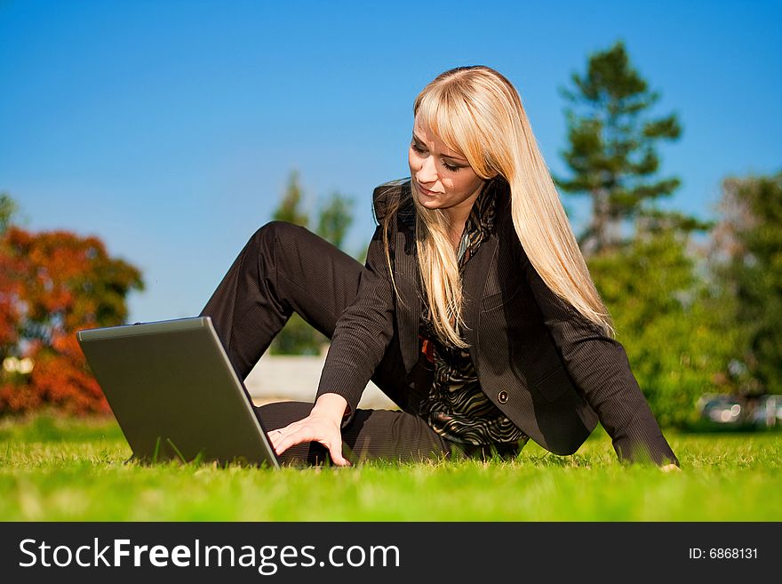 Young blonde businesswoman working on laptop computer in a meadow