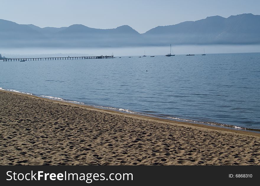 Lake shore with boats and pier in the background, mountains and fog in the distance. Lake shore with boats and pier in the background, mountains and fog in the distance.