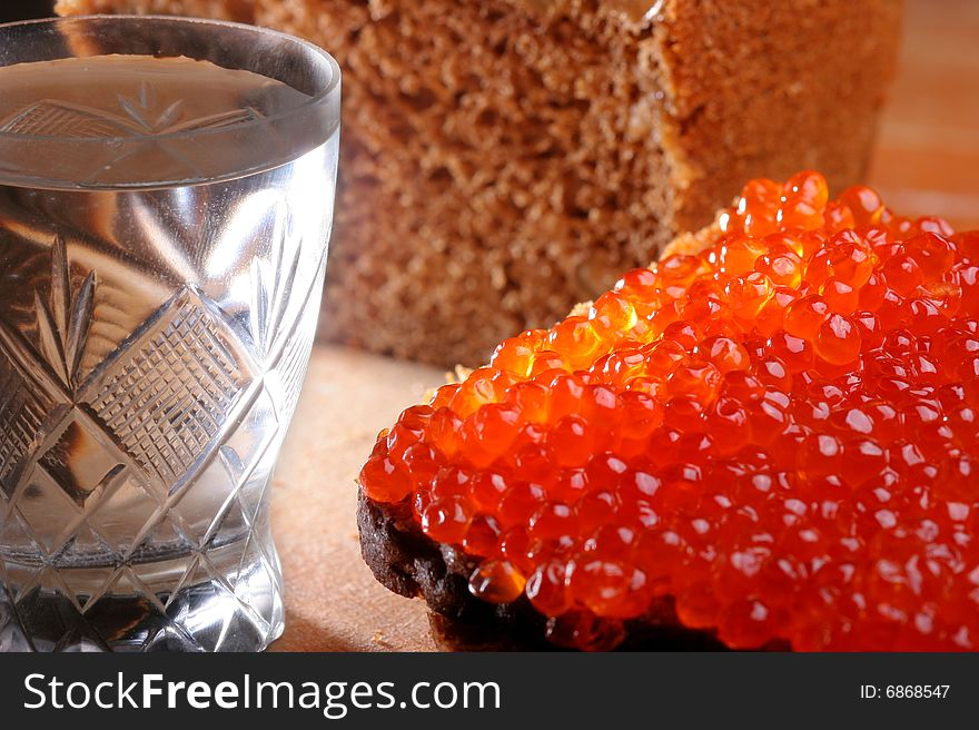 Red caviar, brown bread on a wooden board. Vodka is in a wineglass.