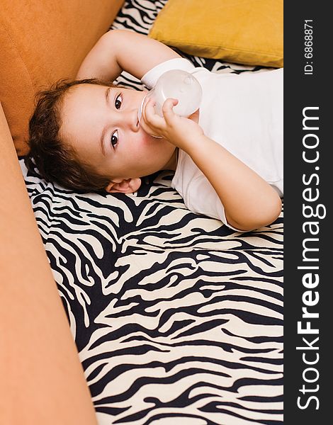 Small boy drinking milk from a bottle lying on a sofa