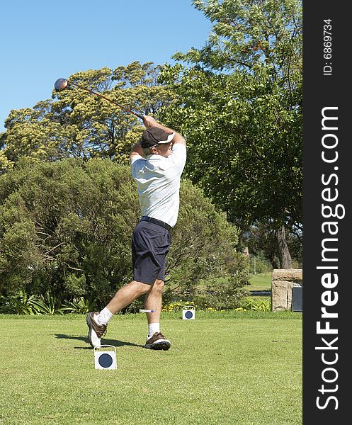 Senior golfer hitting the ball off the tee box. Peg flying past the left leg. Nice summer day