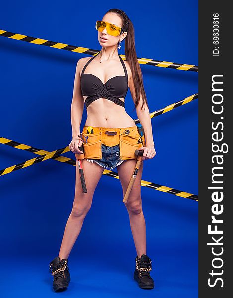 Brunette Builder On A Blue Background With An Electric Tool In The Hands Of