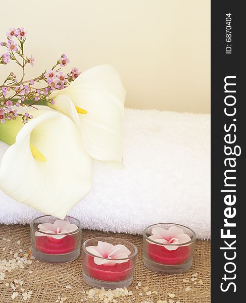 Relaxing spa scene with a white rolled up towel, white lillies, beautiful handmade candles and bath salts