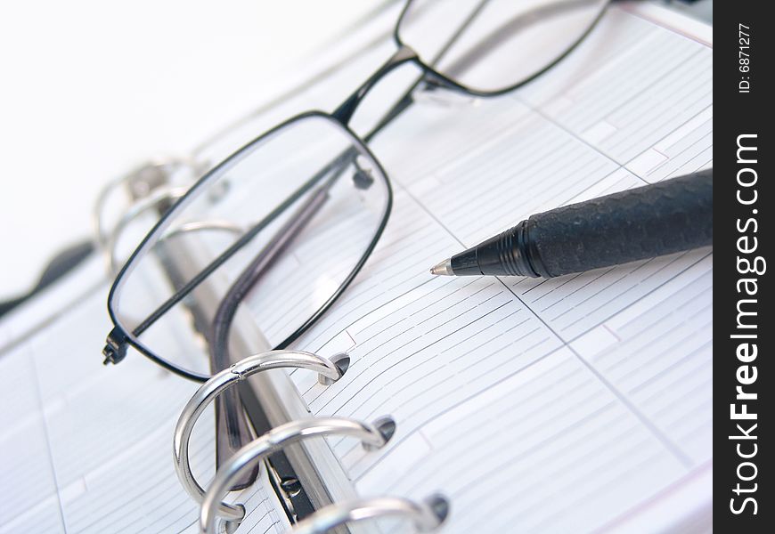 Silver cell phone, pen, and glasses on planner. Silver cell phone, pen, and glasses on planner