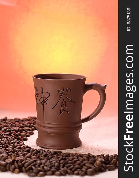 Cup of coffee stands on a sackcloth with coffee-beans and orange background looks like the sun. Cup of coffee stands on a sackcloth with coffee-beans and orange background looks like the sun