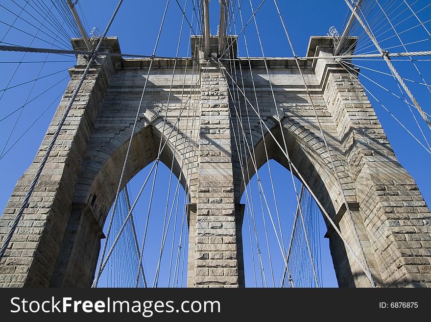 Brooklyn Bridge's arches and cables against the blue sky.
