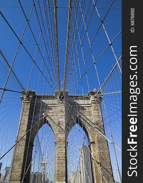 Brooklyn Bridge's arches and cables against the blue sky.