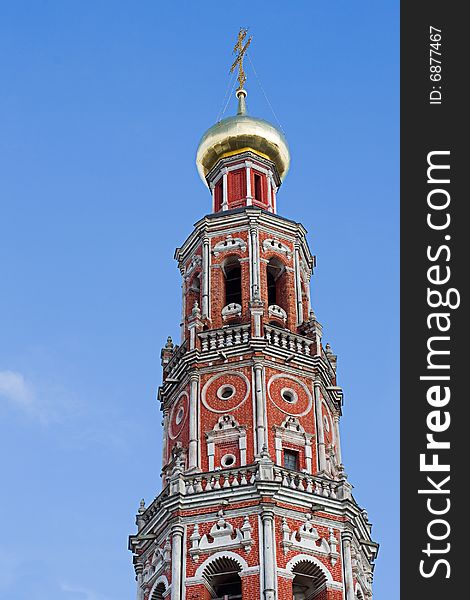 Against the blue sky a high belltower from a red brick, with a gold dome