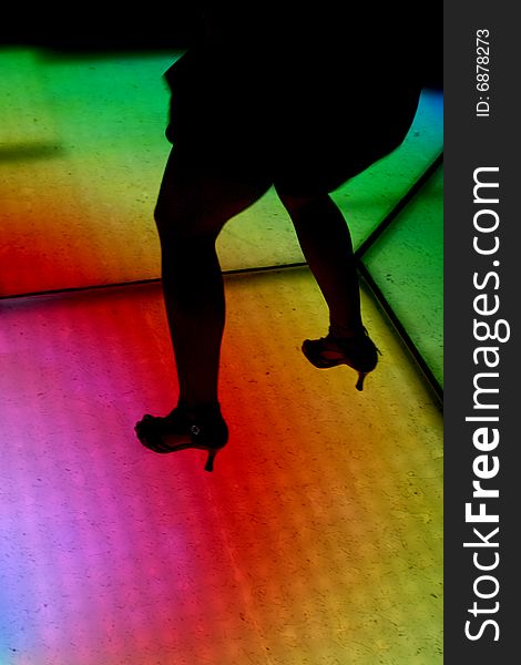 Colorfully lit dance floor, with human silhouettes in motion, dancing
