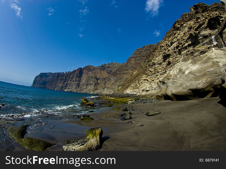 Volcanic rock cliffs and black sand on an ocean beach. Volcanic rock cliffs and black sand on an ocean beach