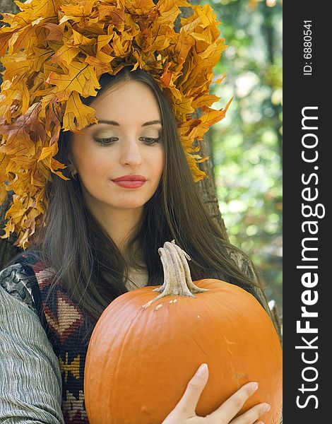 A beautiful young woman wearing a leaf wreath on her head and holding a pumpkin. A beautiful young woman wearing a leaf wreath on her head and holding a pumpkin