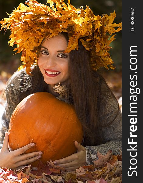 A young beautiful woman  wearing a leaf wreath on her head and holding a pumpkin. A young beautiful woman  wearing a leaf wreath on her head and holding a pumpkin