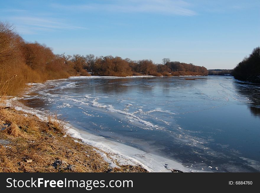 Blue sky and clouds reflection on icy cold river and brown bare bushes on the bank. Blue sky and clouds reflection on icy cold river and brown bare bushes on the bank