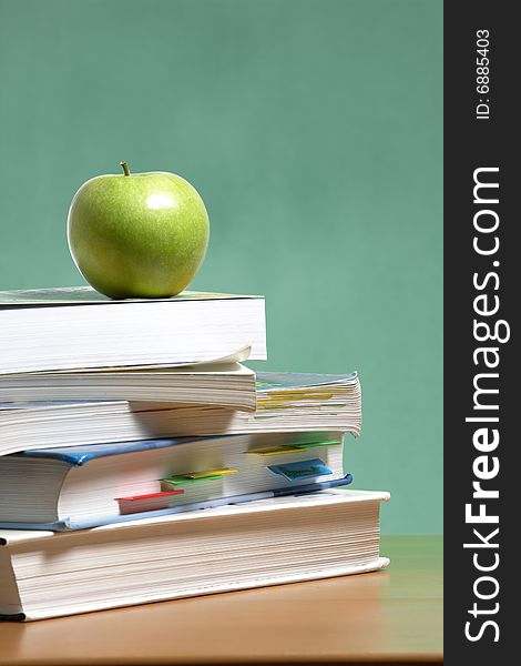 An apple on a stack of books on the teachers desk. An apple on a stack of books on the teachers desk