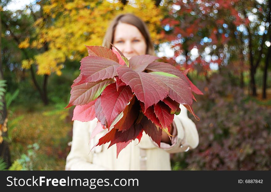 Young woman holds bouquet of autumnal leaves