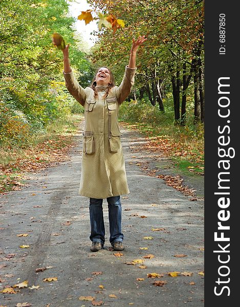 Happy young woman tosses up yellow leaves