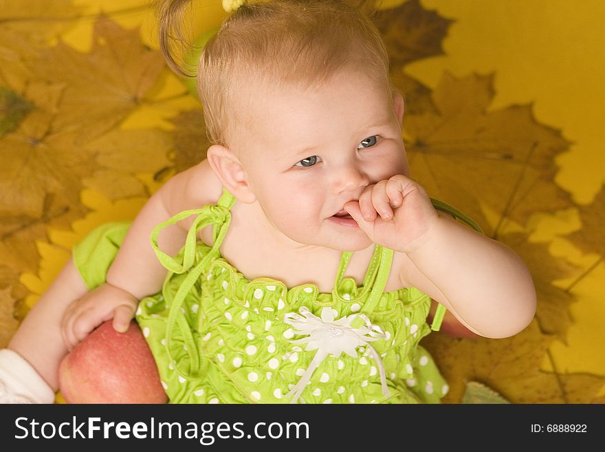Baby with leaves and apples on yellow ground